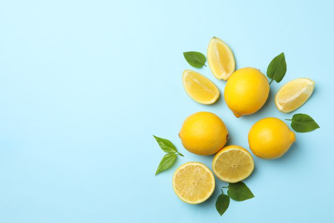 Fresh lemons with leaves on blue background, top view. Ripe fruit