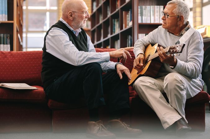 Two mature men sitting on couch and playing guitar together