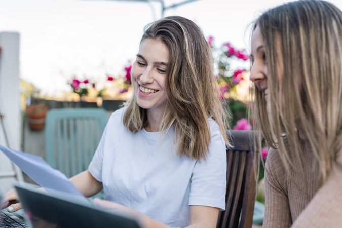Two smiling friends comparing their notes and chatting about what was written on the laptop.