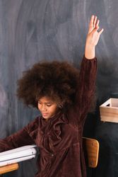 Black girl with raised hand in classroom during lesson