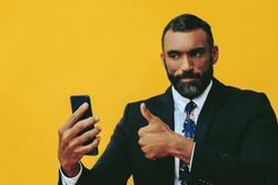 Serious Black businessman in suit giving thumbs up at smartphone screen
