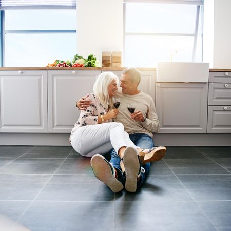 Square shot of smiling mature couple drinking red wine together on kitchen floor