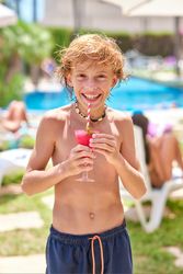 Shirtless boy smiling and holding drink at resort