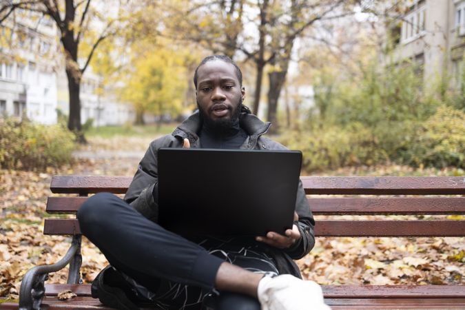 Black Man Having Online Discussion on Laptop in Playground Setting.