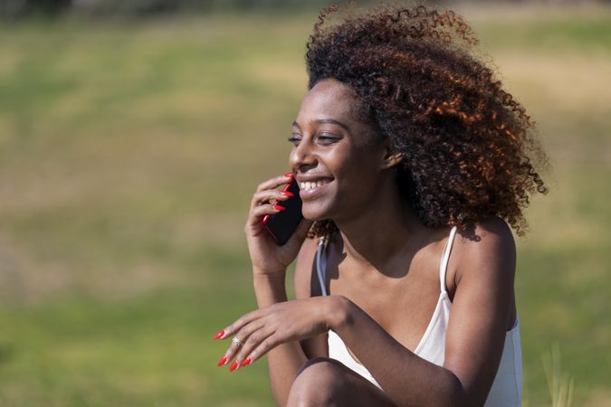 Female in light summer dress sitting in park having fun conversation on her phone