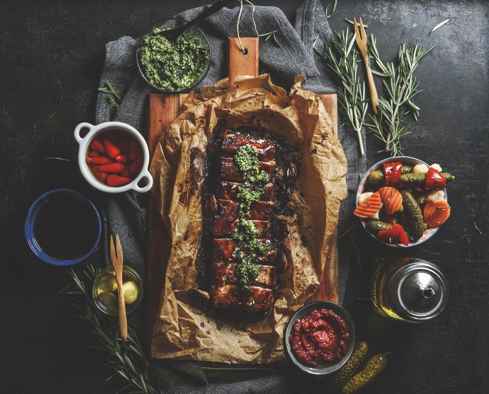 Roasted BBQ ribs with homemade pesto, pickled vegetables, sauces and rosemary on dark concrete kitchen table