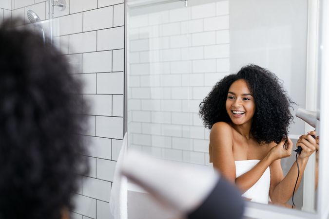 A Black woman blow drying her hair in front of a mirror