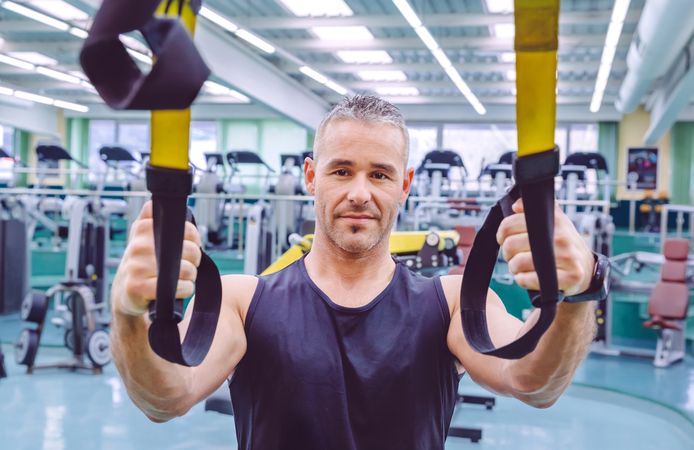 Fit man standing with suspension ropes in gym