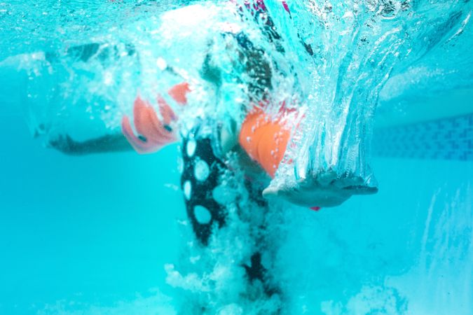 Underwater shot of a girl with arm floats diving in the pool