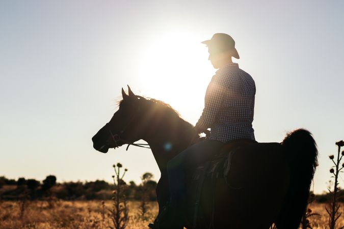Man in hat riding a horse in the countryside at sunset
