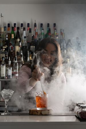 Smiling bartender stirring a cocktail surrounded by smoke