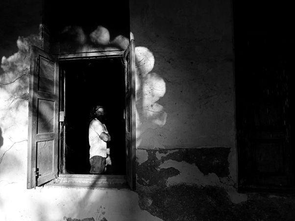 Grayscale photo of man standing by window