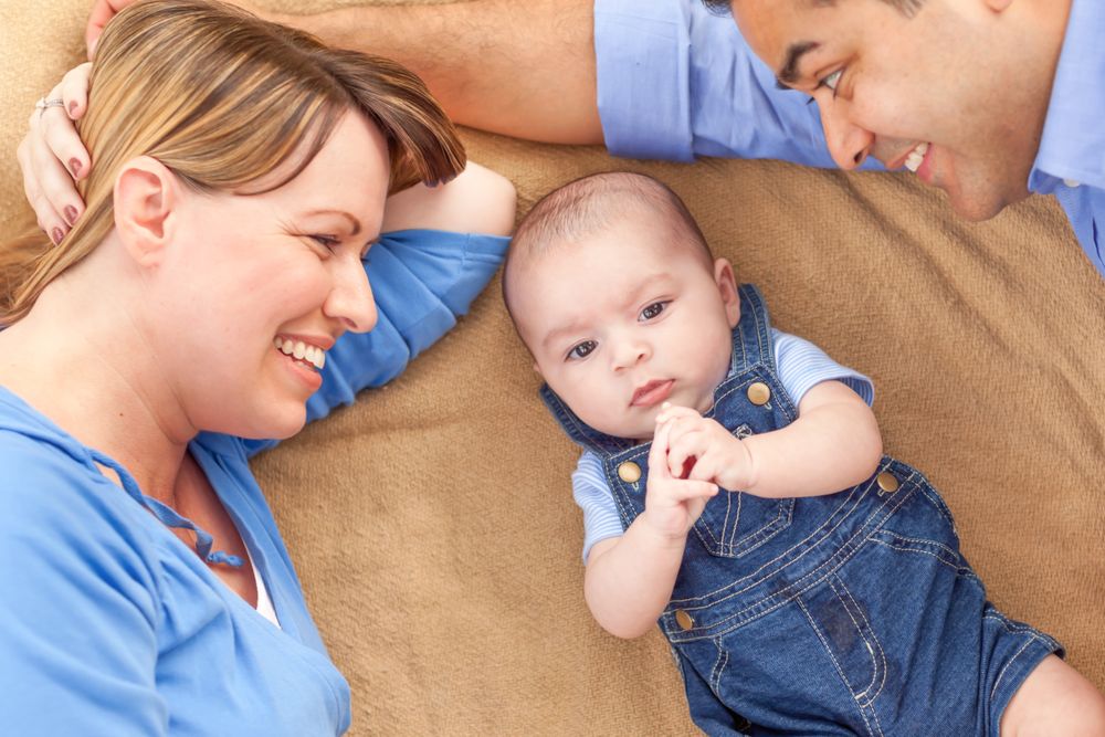 Young Couple Laying With Their Infant On A Blanket