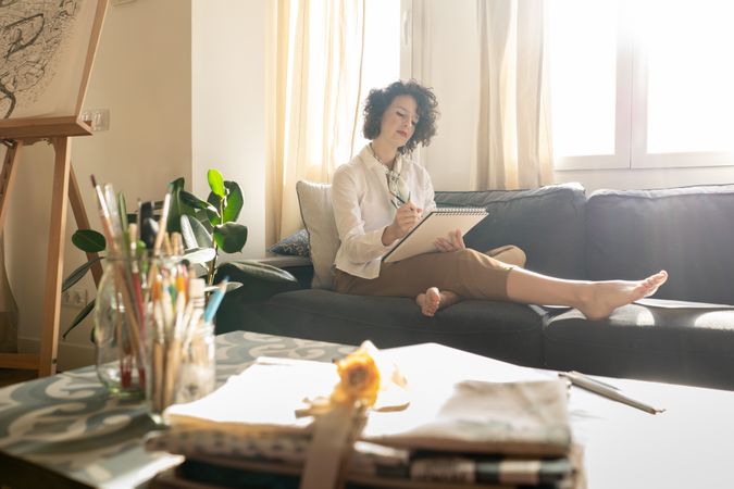 Woman writing on paper on sofa in room