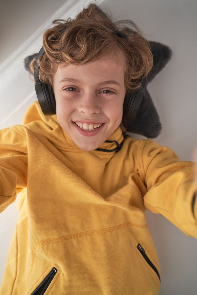 Cheerful child in headphones listening to music and taking selfi