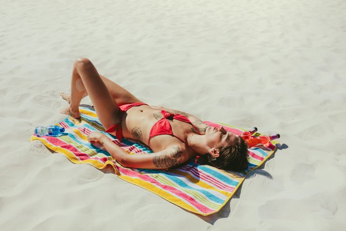 Fit woman in swimsuit lying on a towel sunbathing at the beach