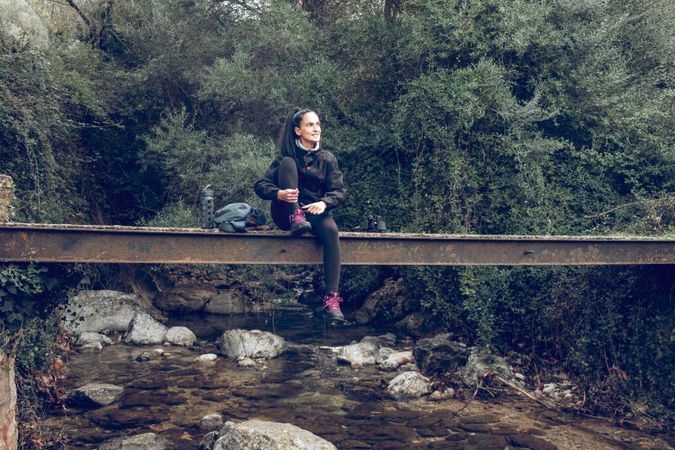 Smiling female relaxing on old bridge during hiking trip in