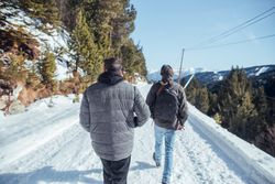 Men walking on road between hills with trees in winter