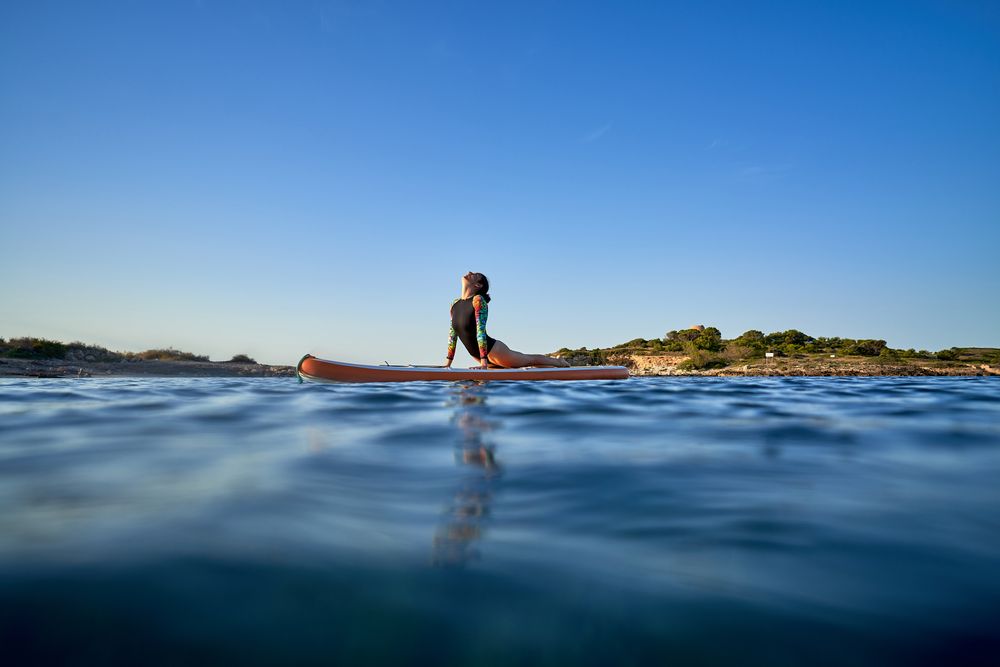Fit sportswoman taking Cobra pose on SUP board in sea