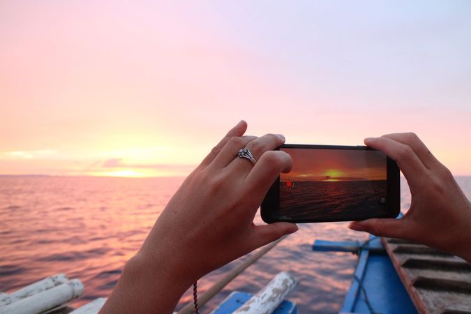 Woman holding smartphone shooting the sea during sunset