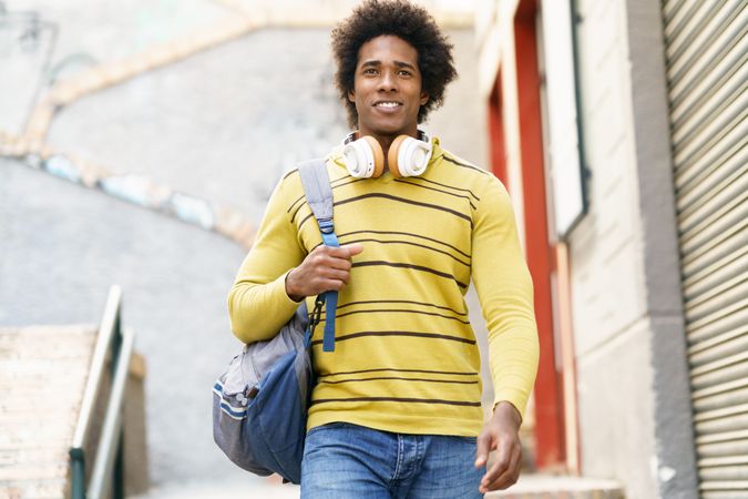 Smiling man in yellow shirt and headphones walking down stairs outside
