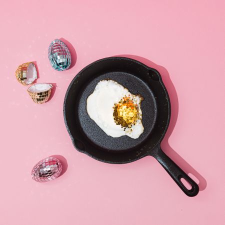 Shiny disco ball eggs and golden glitter yoke in cast iron on pastel pink background
