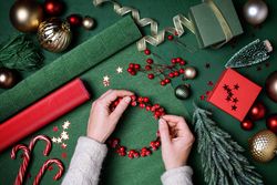 Hands creating a berry wreath for Christmas on green background
