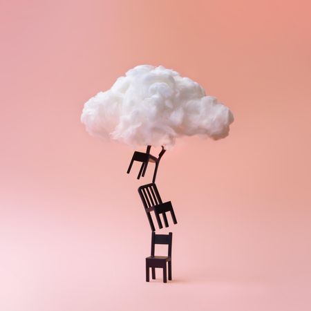 Stacked chairs towards clouds against coral color background