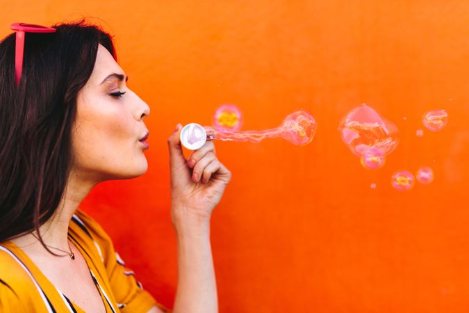 Young woman having fun blowing bubbles against orange wall