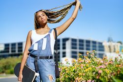 Serious female in denim overalls holding skateboard on campus