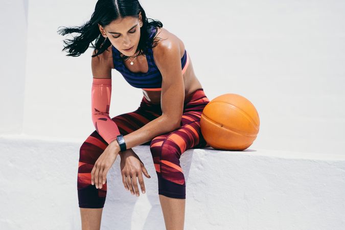 Slender woman sitting with basketball on wall ledge