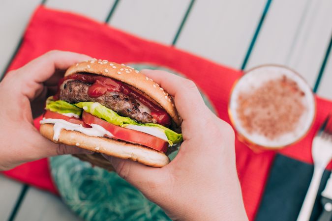 Hands holding a cheeseburger with lettuce and tomato