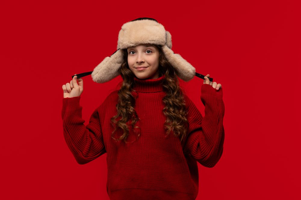 Smiling girl in fur hat holds ear flaps of hat
