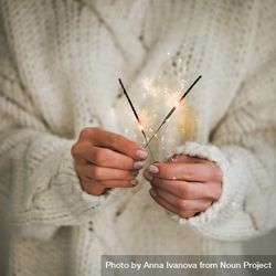 Woman holding two sparklers,  sweater, square crop 0vj7x0