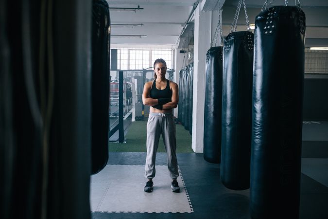 Portrait of female boxer surrounded by punching bags in studio