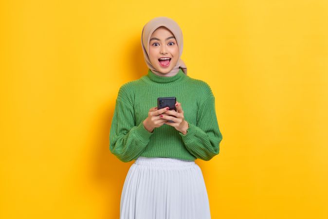 Very happy woman in headscarf smiling and looking up from her smart phone