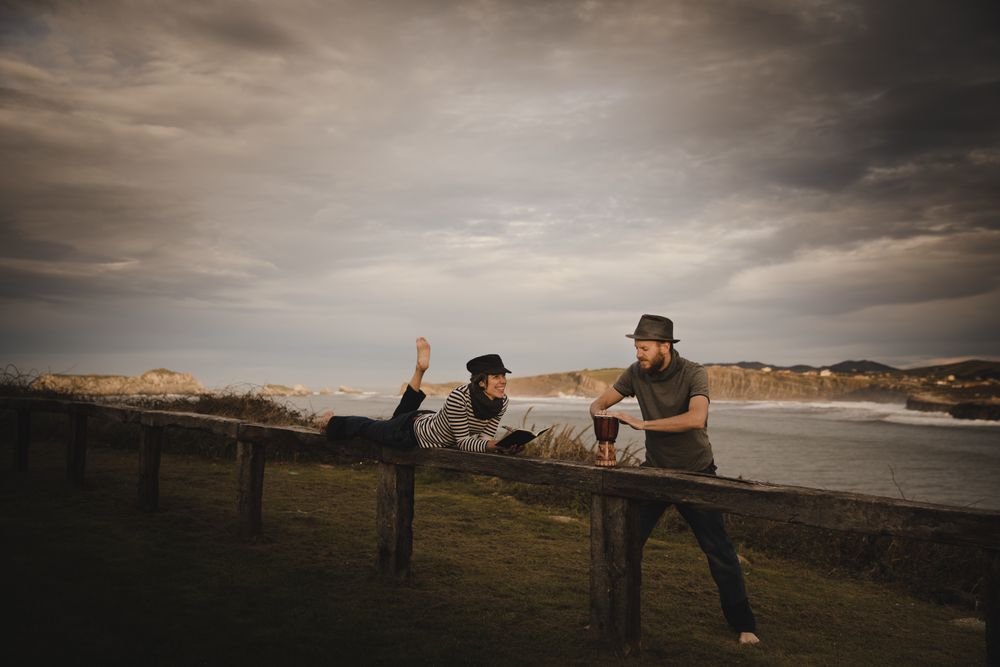 Man plying on drum near woman with notebook on bench on shore
