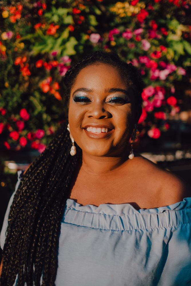 Joyful trendy Black woman standing beside blossomed tree