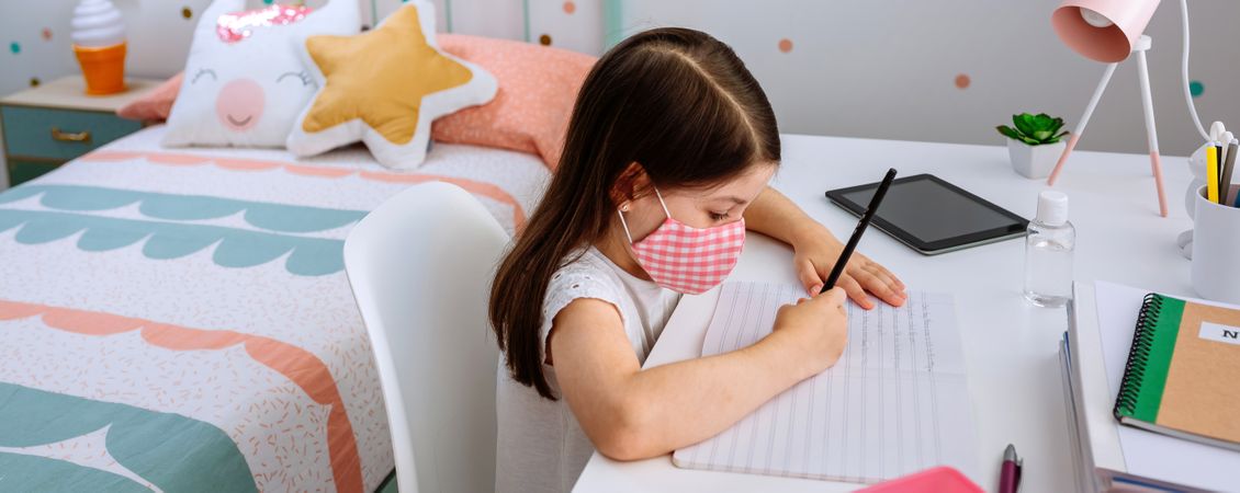 Girl with mask doing homework in her bedroom