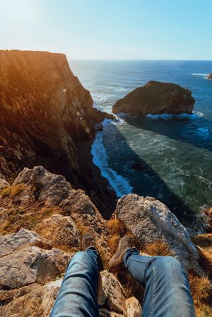 Person sitting on cliff near water