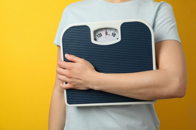 Woman holds scales on yellow background. Weight loss