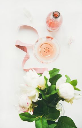 Top view of glass of pink rose wine, and bottle with flowers and ribbon