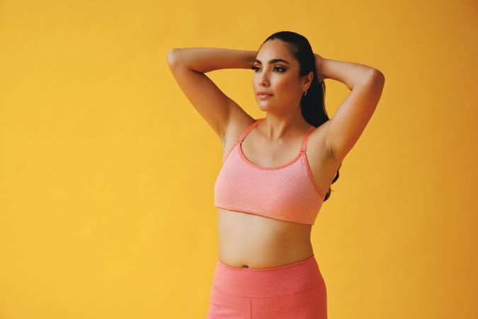 Hispanic woman in yoga clothes looking in the distance with hands on her head, copy space