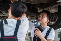 Two male auto repairmen working on undercarriage of vehicle