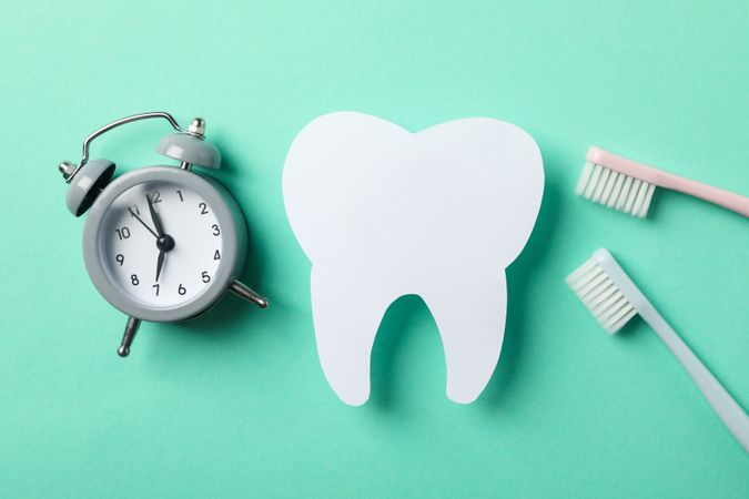 Clock, tooth and toothbrushes on mint background, top view