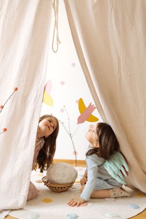 Cute little girls with angel wings costume sitting on mat and playing with paper birds