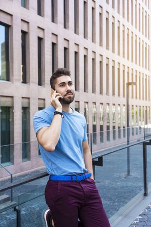 Young bearded man talking on mobile phone while leaning outside