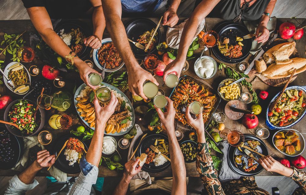 Group of people at wooden table with meze feast, serving toasting with white aperatif