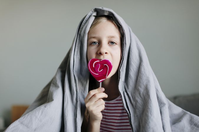 Wide view of young girl holding a pink heart shaped lollipop