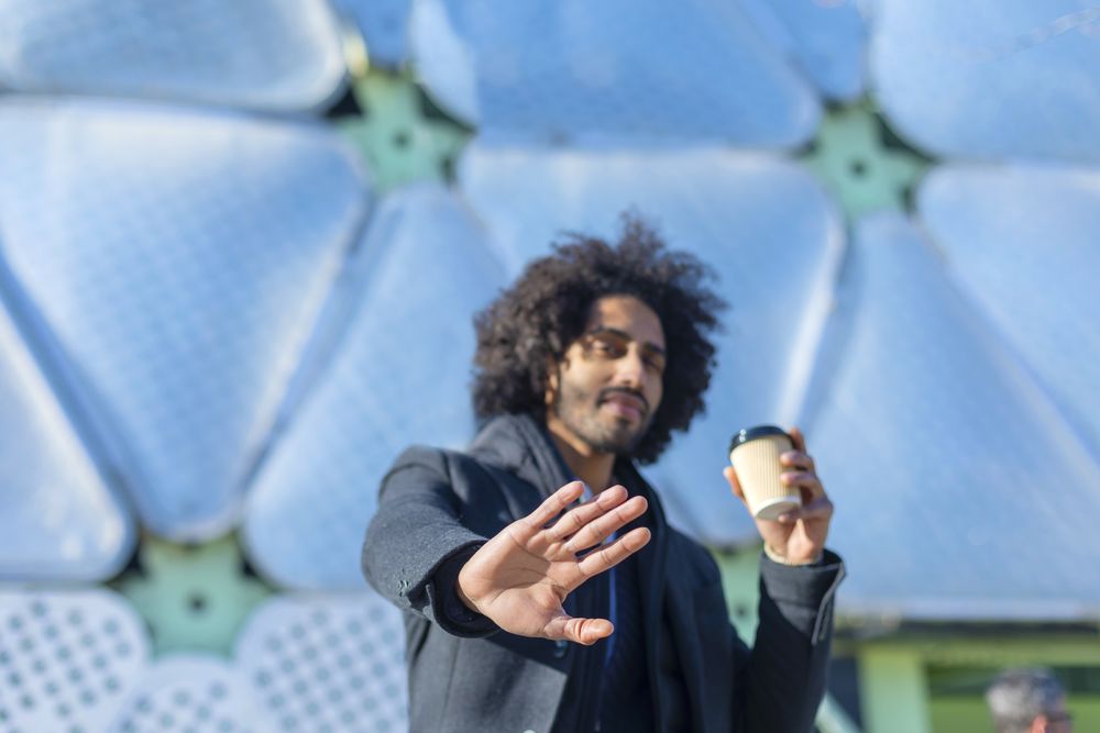 Black man in jacket with warm beverage making stop gesture with hand outside